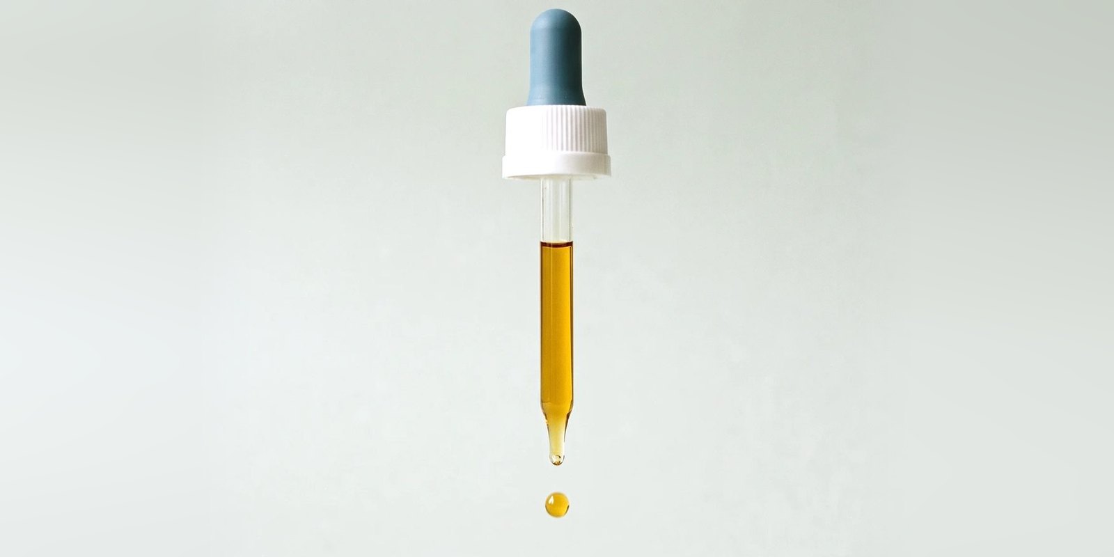 Conta-gotas com óleo dourado soltando uma gota